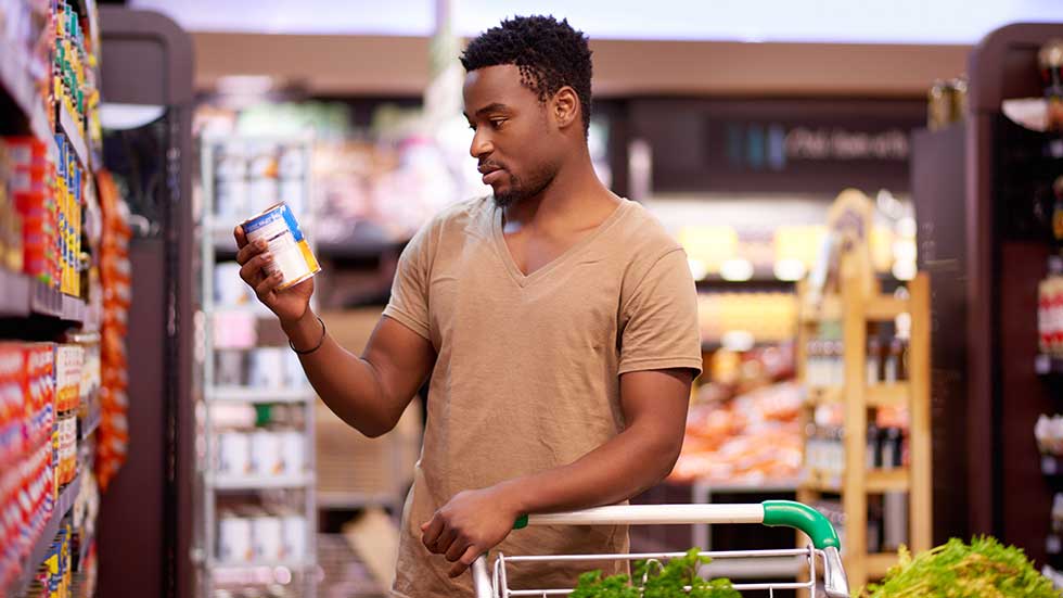 Young man picks up a can while shopping in a modern supermarket.