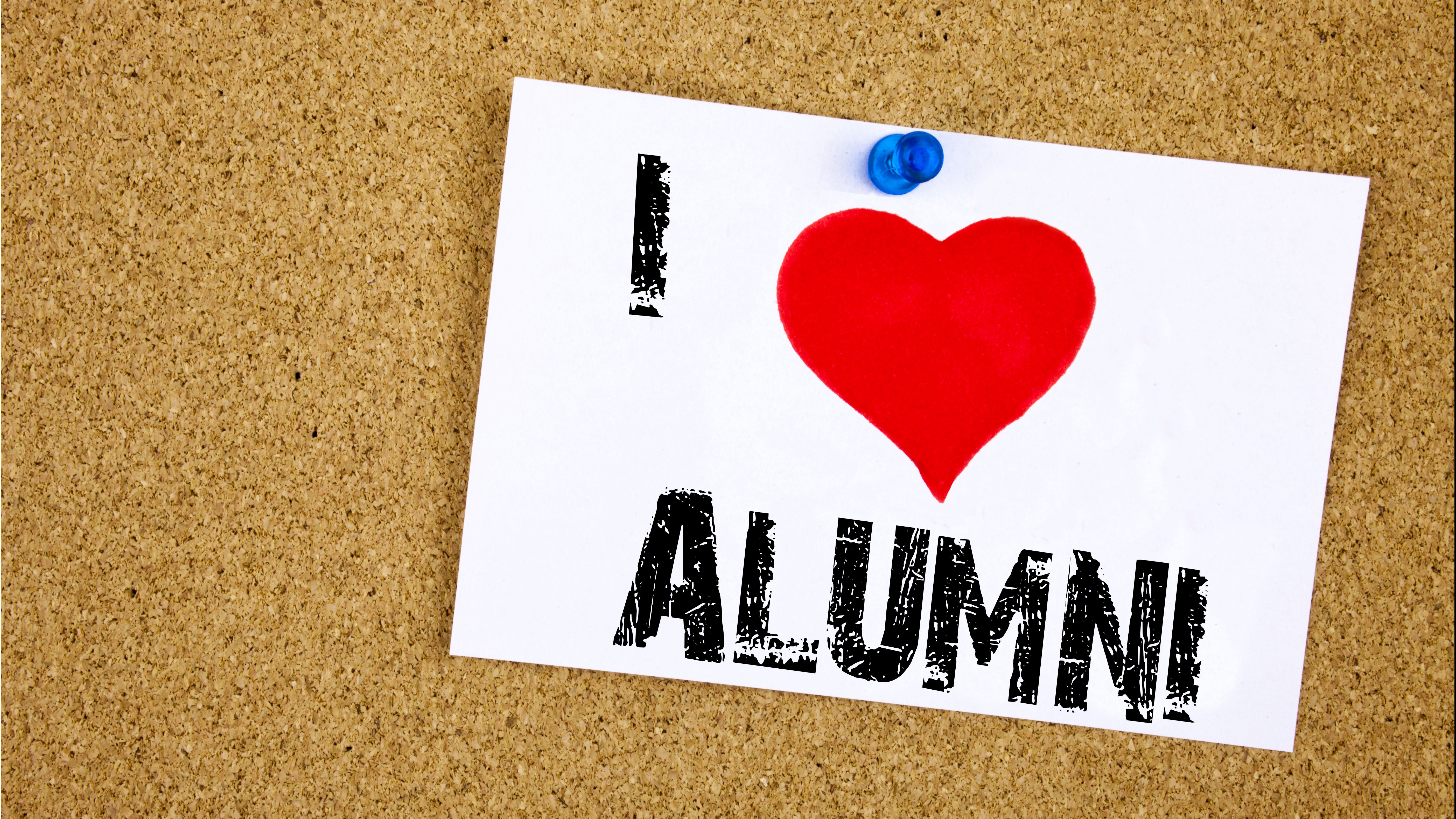 Eine Postkarte mit der Aufschrift "I love alumni" hängt an einer Pinnwand. 