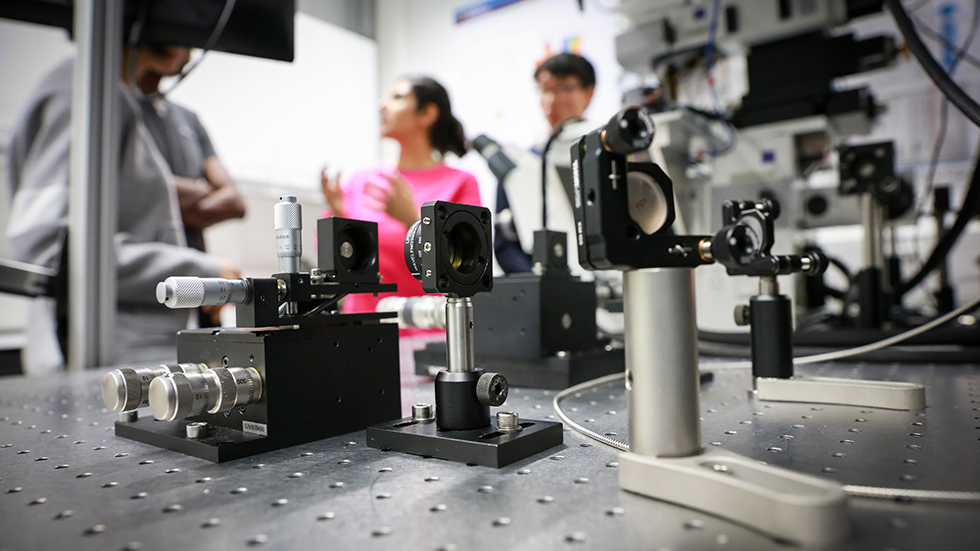 Researchers are standing close to a microscope. 