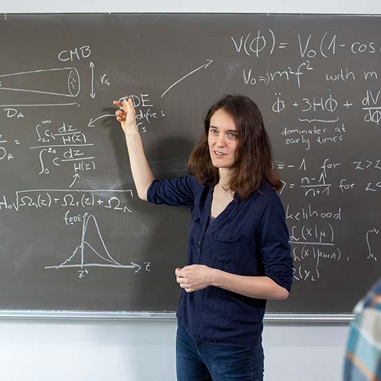 A female scientist at the Max Planck Institute for Extraterrestrial Physics is presenting a formula on a blackboard to her colleagues. 