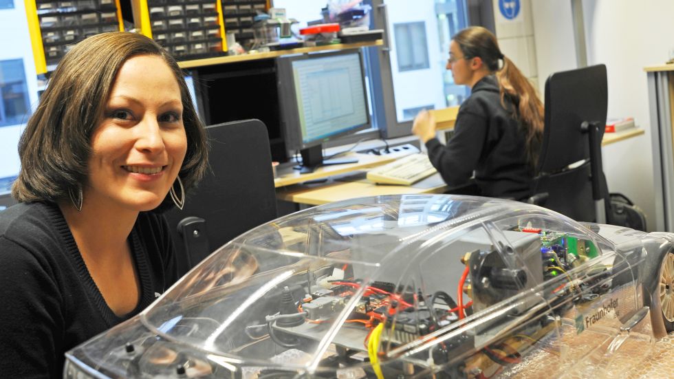 A researcher in front of a model car with Fraunhofer's logo