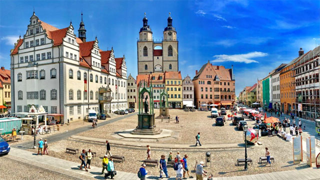 The market place of the German city Wittenberg with a church and old houses around it.