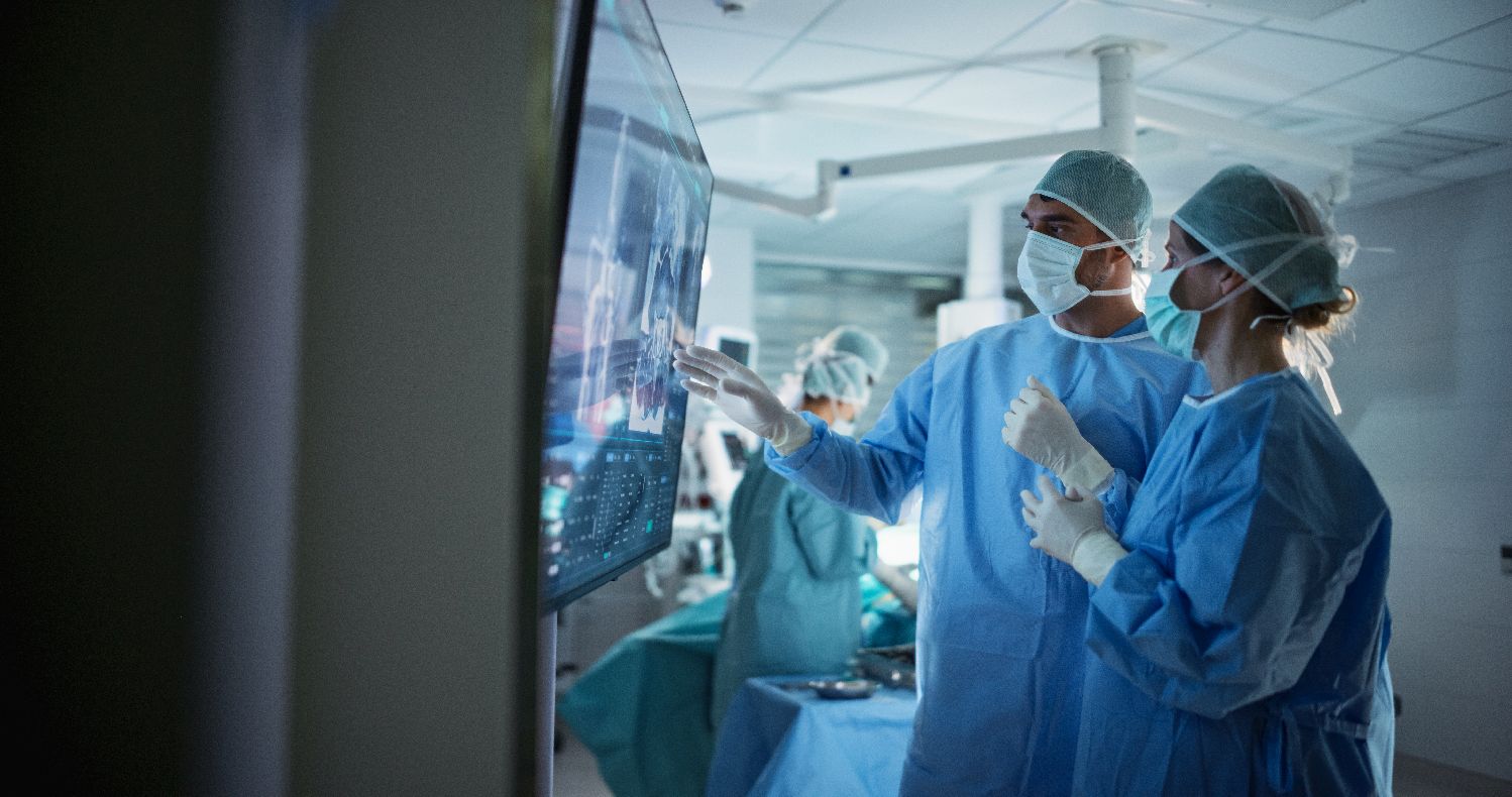 Male and Female Surgeons Analyze Scans on a Digital Monitor, Planning Surgical Strategy in a High-tech Operating Room.