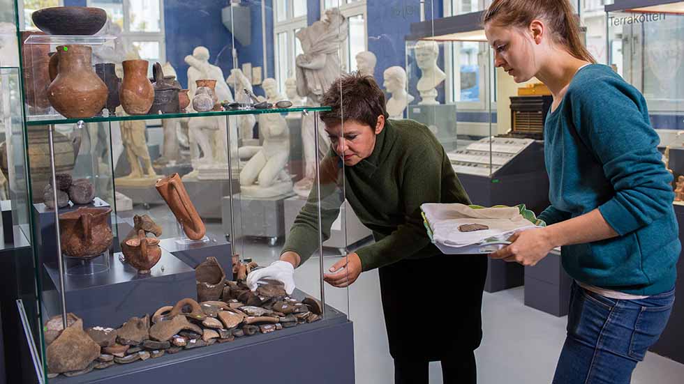A professor and a scientist discuss antique fragments and clay pots.