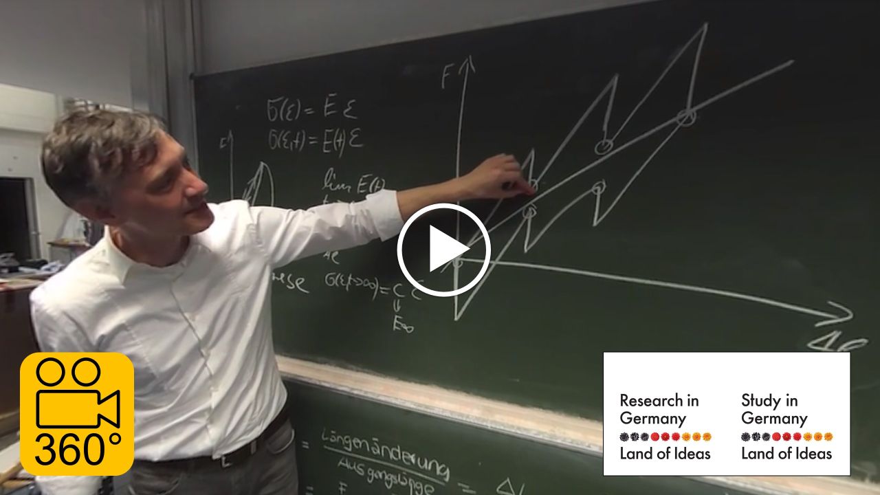 A researcher is standing in front of a blackboard and explaining a graph on it.