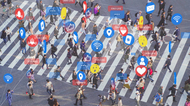 Auf einer großen Kreuzung laufen viele Menschen über einen Zebrastreifen mit Emojis und Icons über ihren Köpfen.