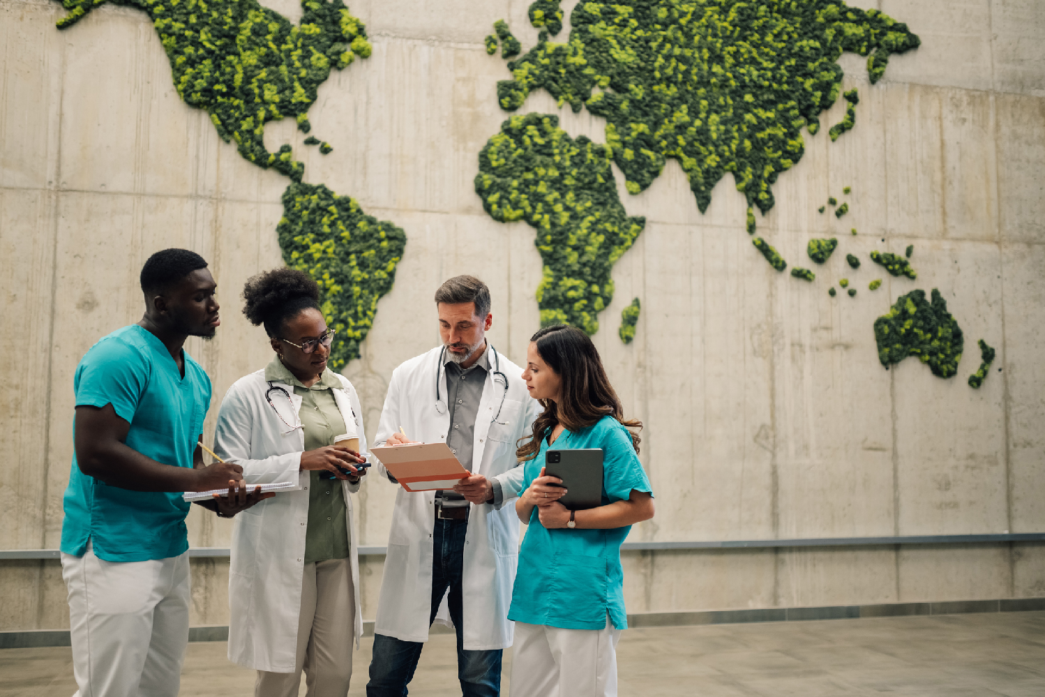A group of professionals in scrucs and lab coats disusses in front of a natural grown world map on a wall