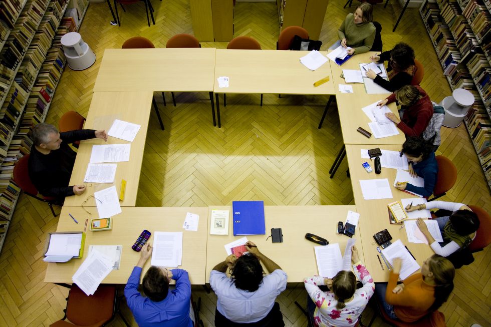 Ten researchers are sitting on tables arranged in a square and working on papers.